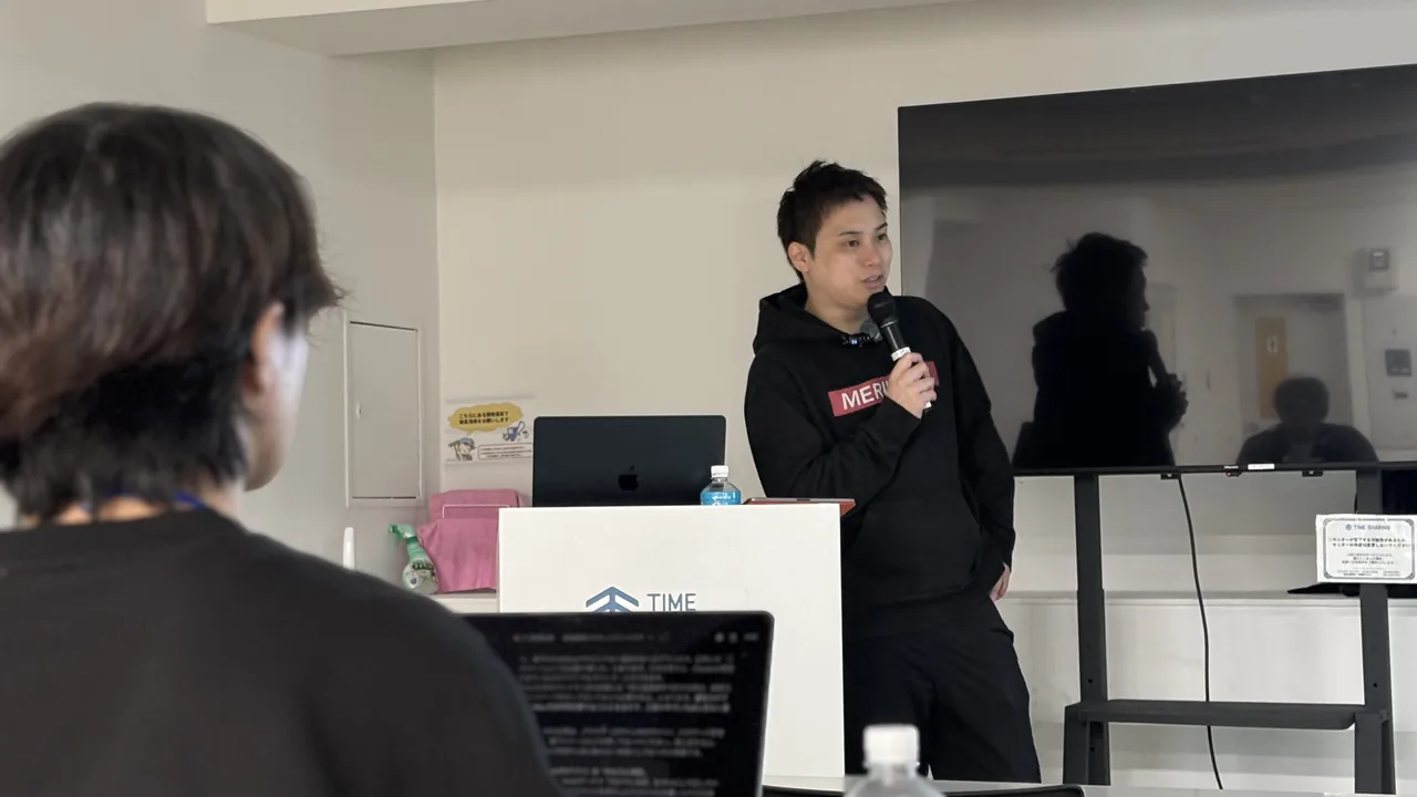 1日目、会場でマイクを持って講義する中島大介と、パソコンを開いて受講する参加者の後ろ姿