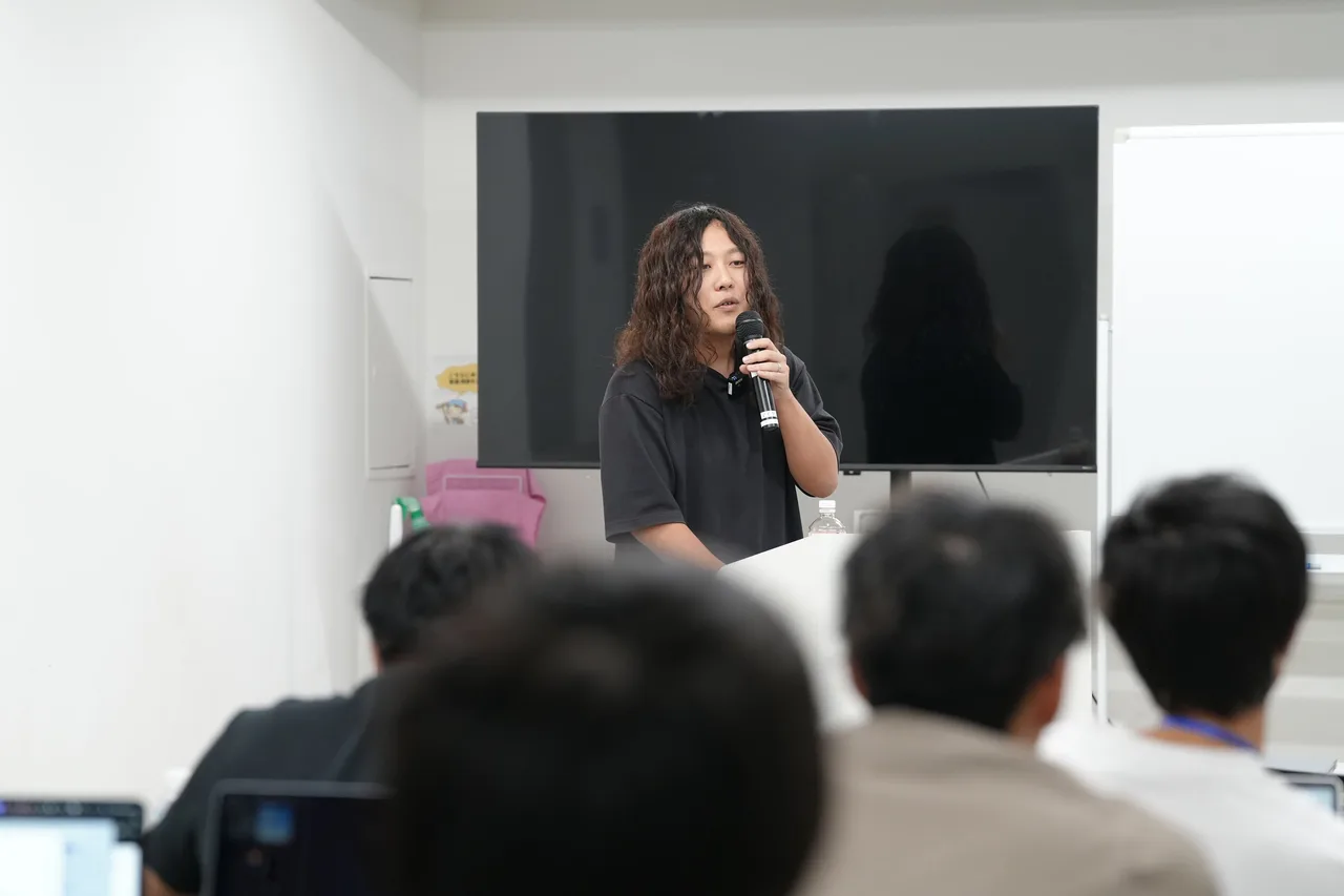 2日目、マイクを持って話す豊蔵翔太様と、手前で受講する参加者の後ろ姿