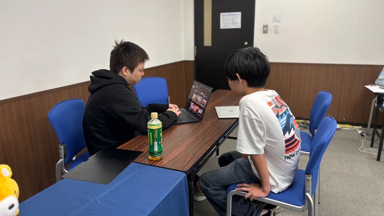 同じパソコンの画面を見ながら、参加者と講師が話すClaude Code合宿の一場面